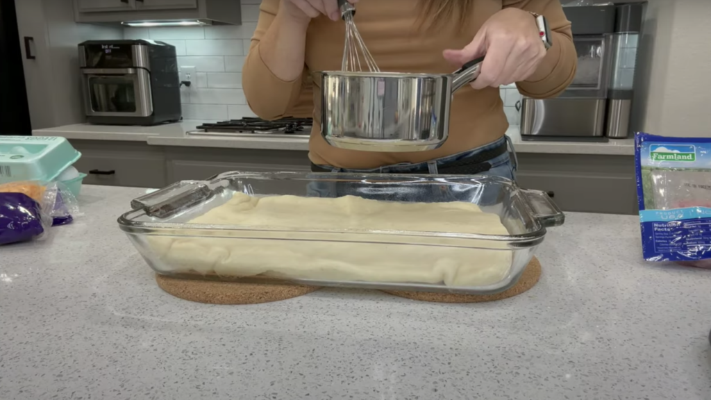 Pizza crust evenly spread along the bottom of the large glass baking dish