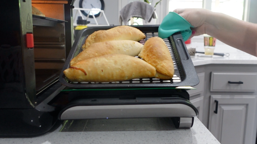 breakfast pockets being pulled out of the air fryer by Lindsay, they are golden brown and crispy