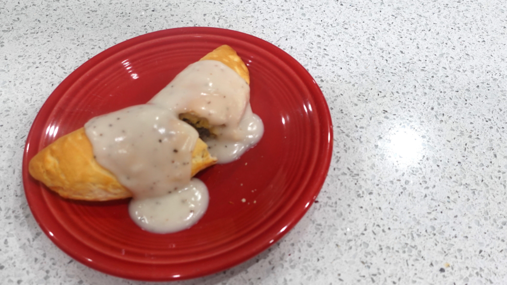 An image of the finished breakfast pocket on a red plate, with gravy drizzled over the top of it