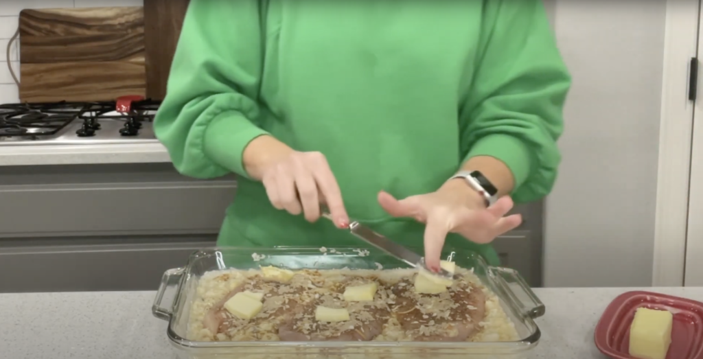 Lindsay placing chunks of butter on top of each chicken breast before placing the dish into the oven.