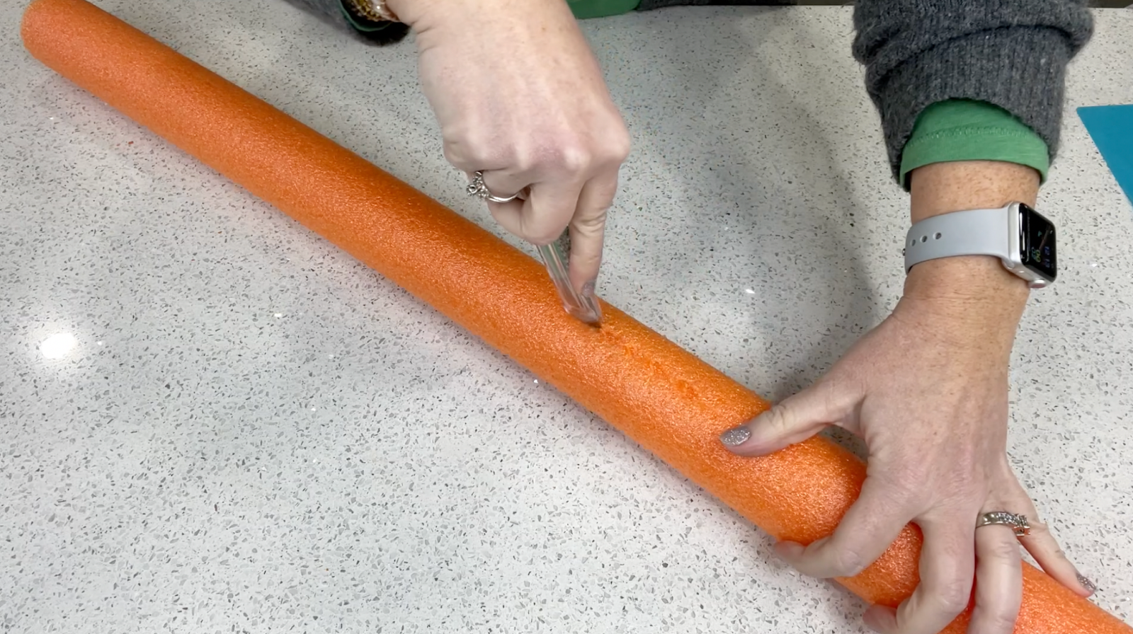 Lindsay cutting an orange pool noodle in half length-wise using a box cutter