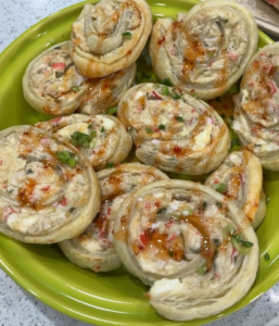 Crab rangoon puff pastry rolls baked golden and topped with sweet Thai chili sauce and chopped green onions on a green serving plate.